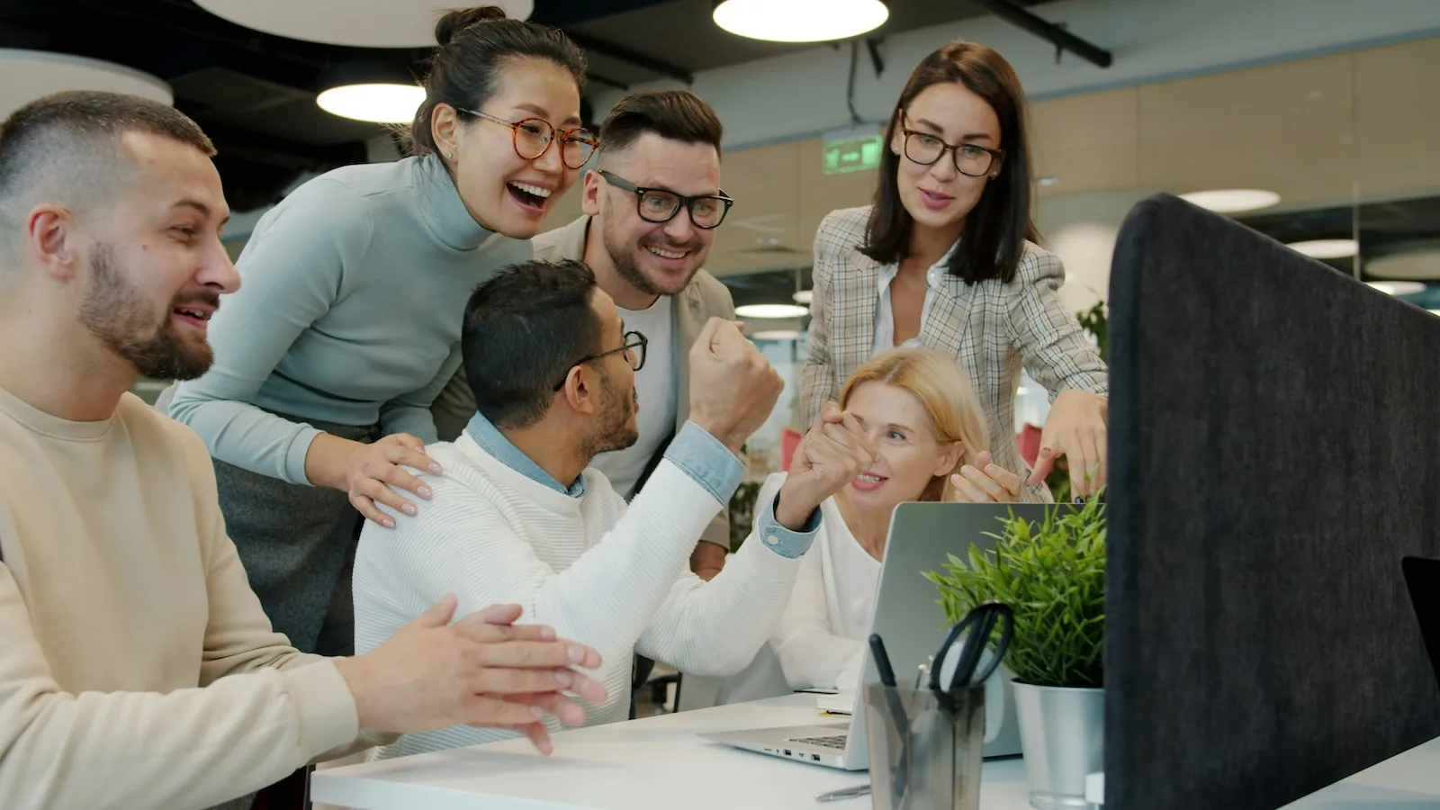 group of supportive employees gathered around computer excited about what they see