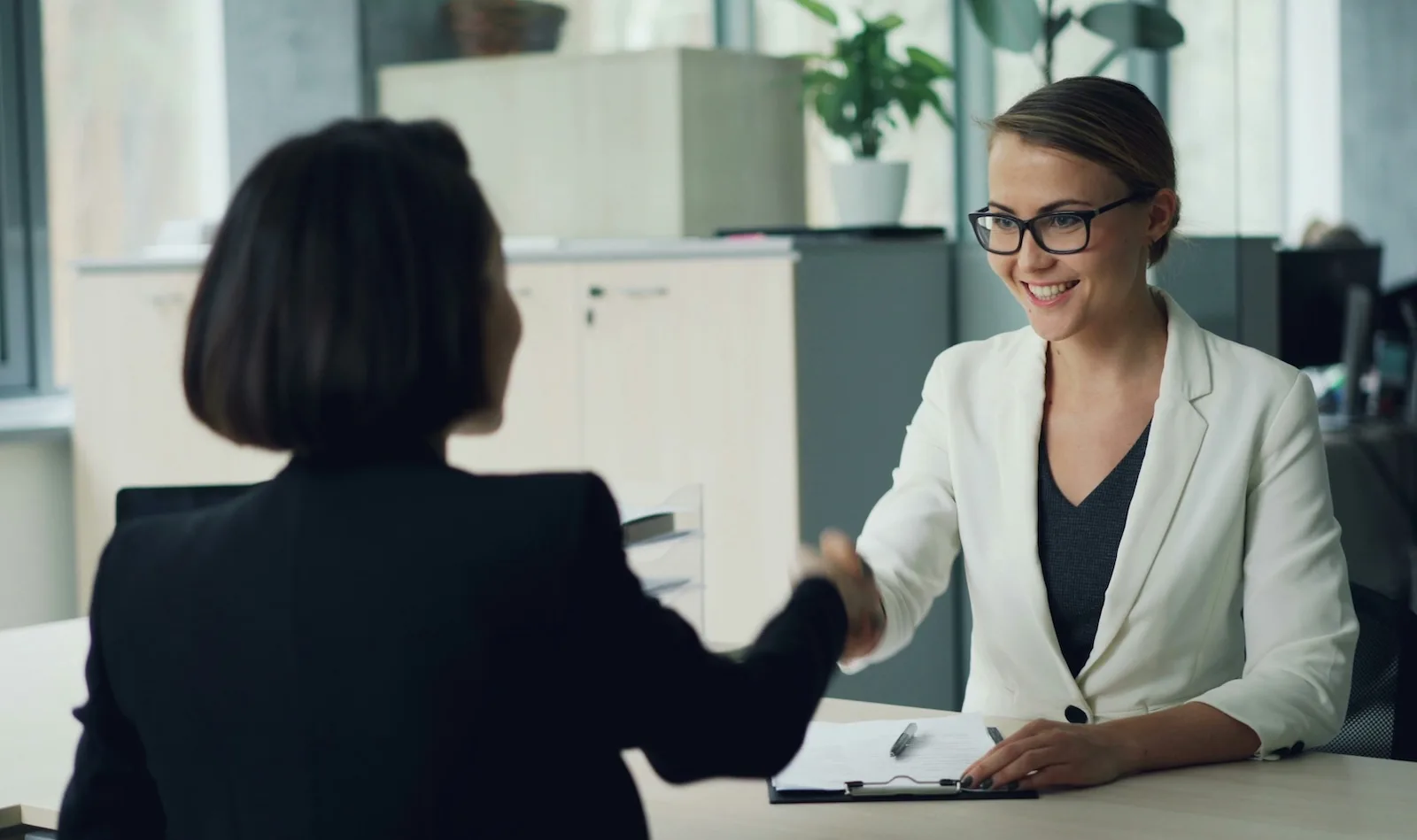 two women shaking hands across a desk two professional women shaking hands across a desk